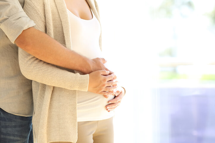 一对怀孕的夫妇站在一起，双手放在女人的肚子上。