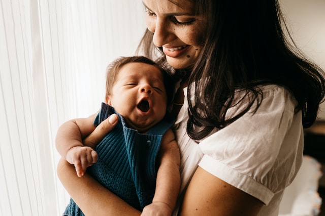一位微笑的女士抱着一个穿着针织连体衣的婴儿