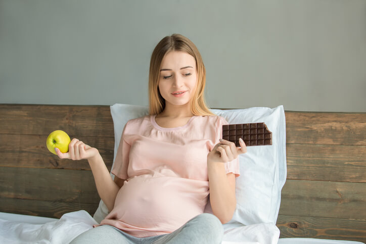 孕妇一手拿着苹果，另一只手拿着巧克力。