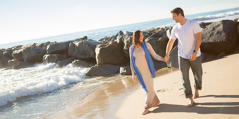 一名男子和一名孕妇手牵手走在海滩上。